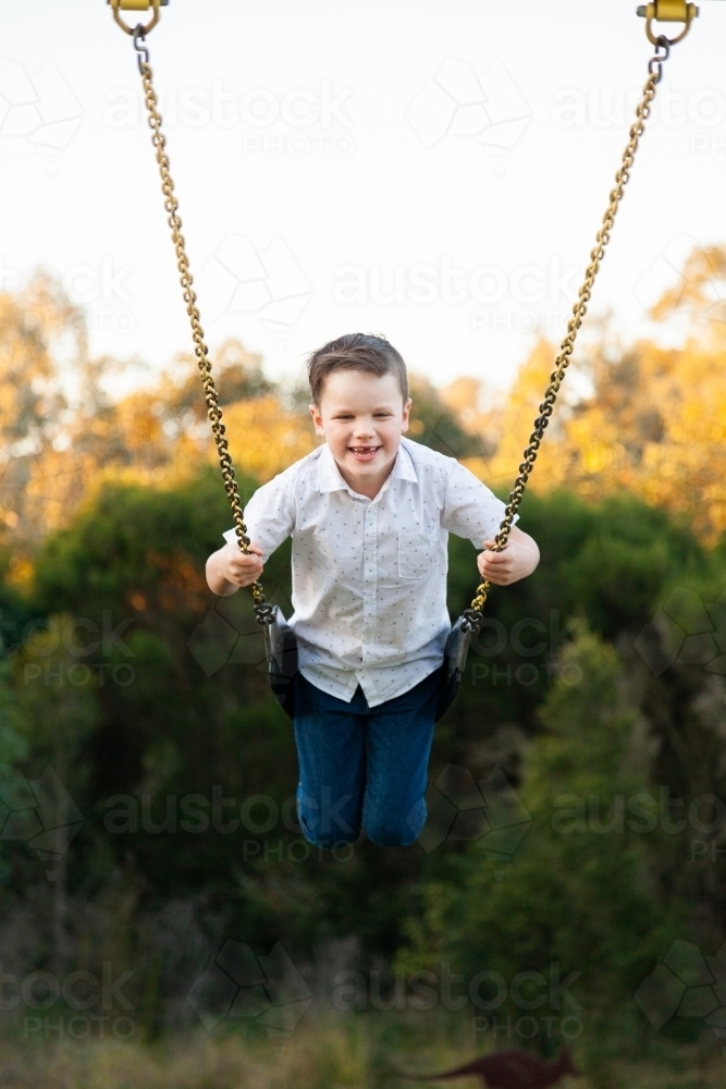 Happy young boy playing on a swing at a park - Australian Stock Image