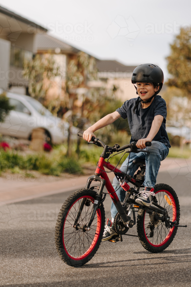 Happy young boy riding his bicycle on the street. - Australian Stock Image