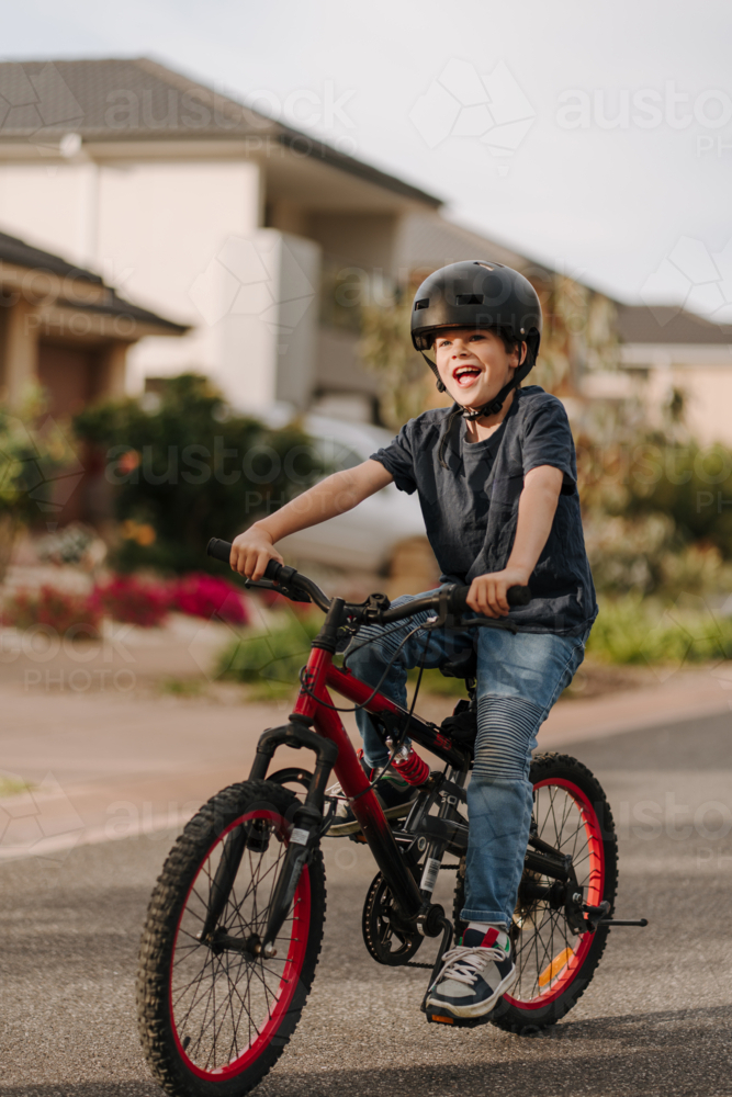 Happy young boy riding his bicycle on the street. - Australian Stock Image