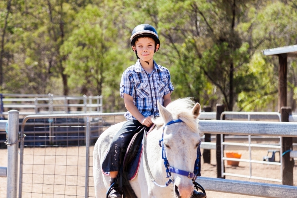 Happy young boy with safety horse riding helmet on horseback during lesson - Australian Stock Image