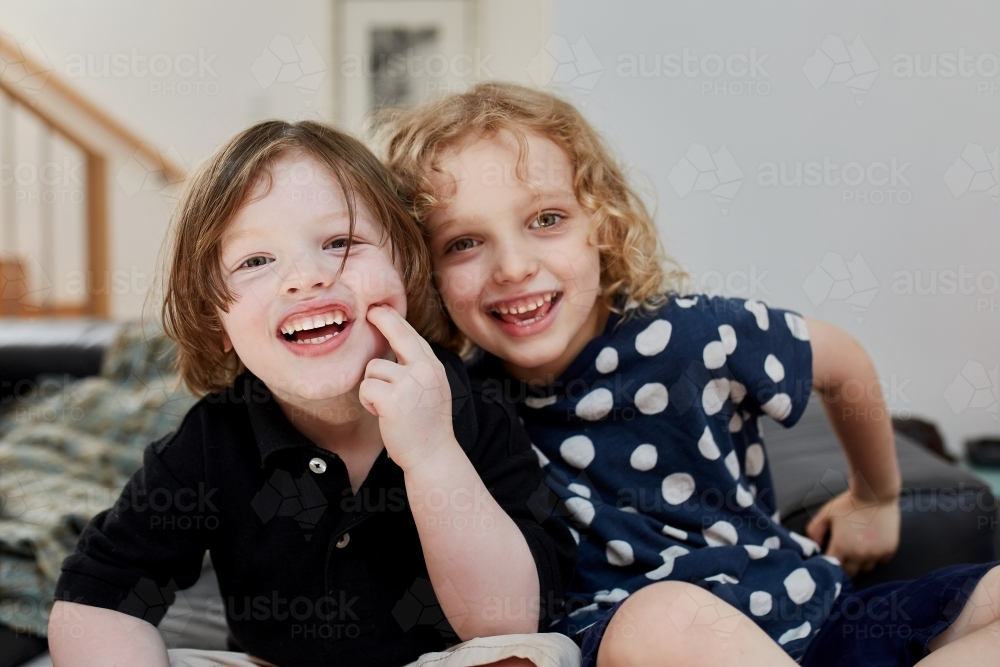 Happy young children smiling while sitting on the couch - Australian Stock Image