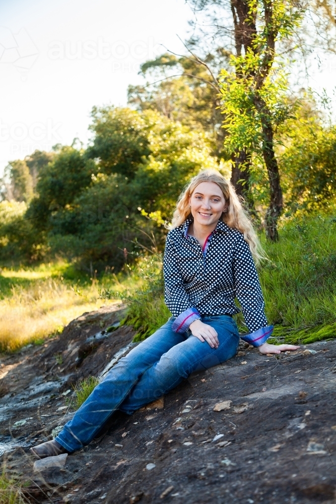 Happy young country woman relaxing in shade by the creek - Australian Stock Image