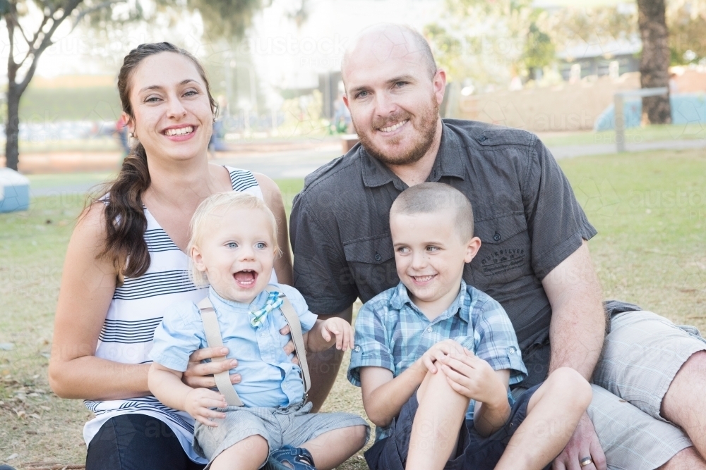 Happy young family smiling for portrait in park - Australian Stock Image