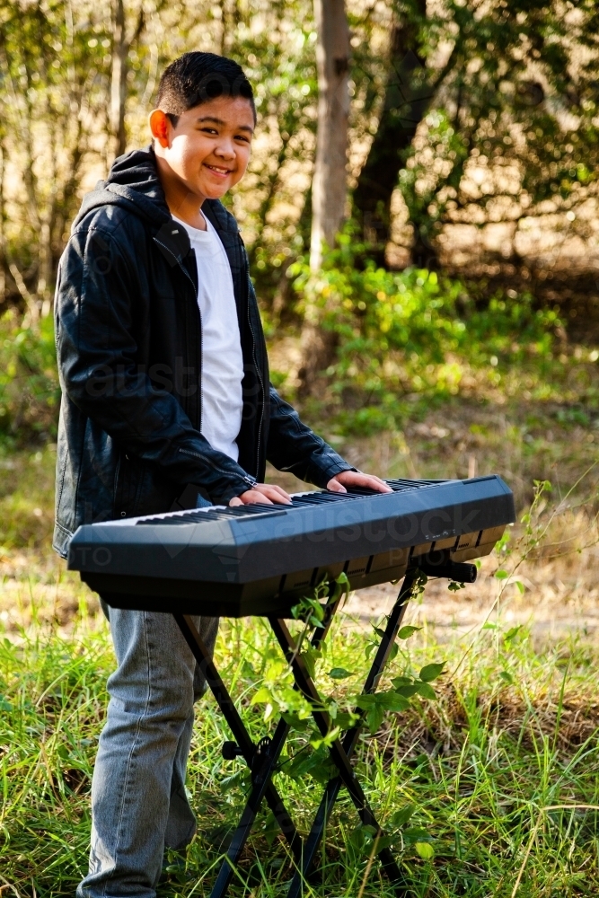 Happy young Filipino boy playing keyboard outside - Australian Stock Image