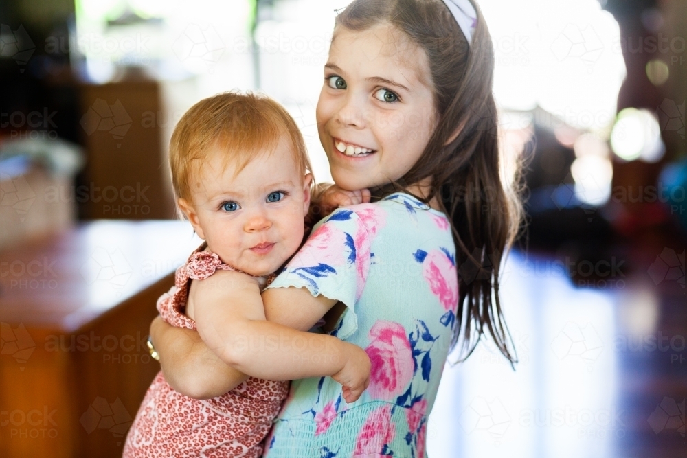 happy young girl picking up and holding baby niece - Australian Stock Image