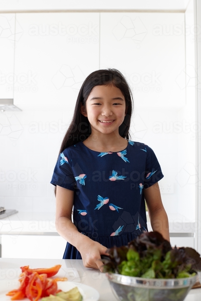 Happy young girl preparing healthy lunch in kitchen - Australian Stock Image