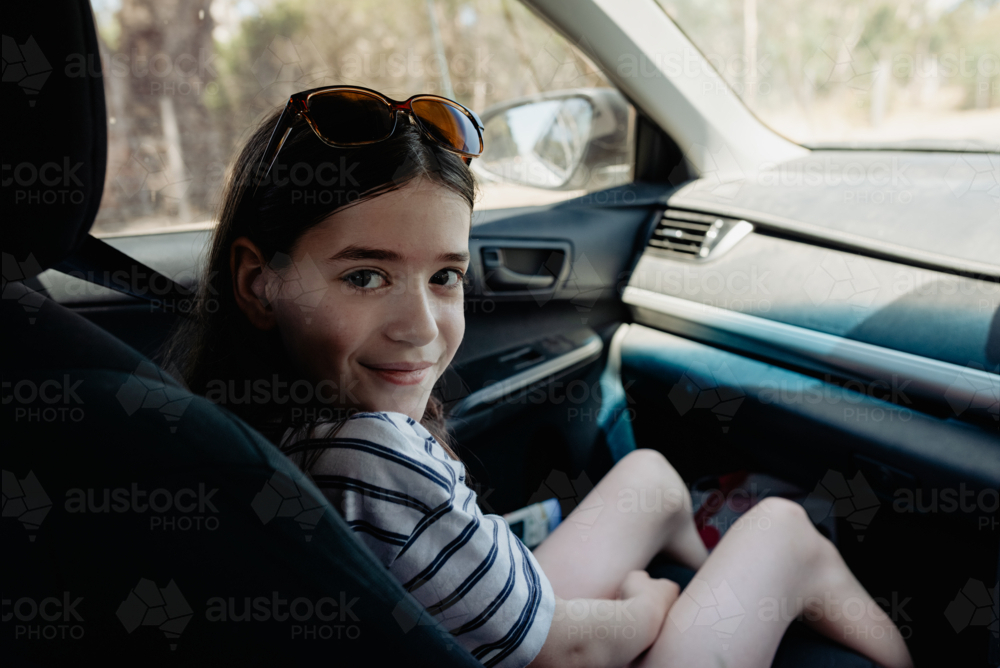 Happy young girl sitting in the front seat of a car looking over her shoulder at the camera - Australian Stock Image