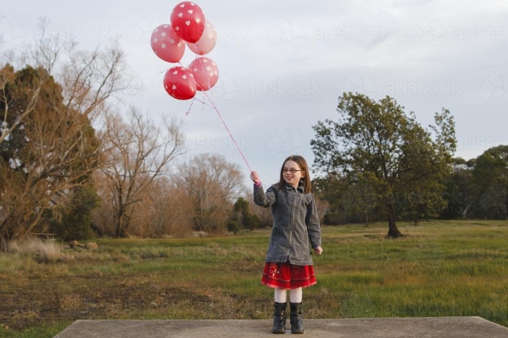 Happy young girl with a bunch of pink balloons outside - Australian Stock Image