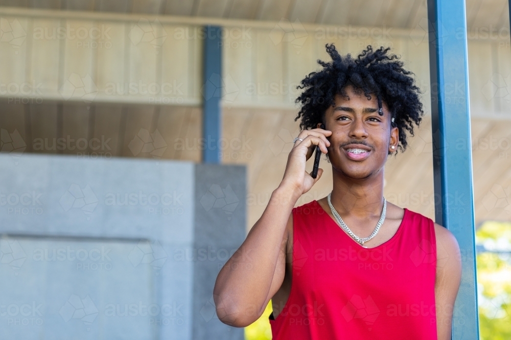 happy young guy talking on smartphone wearing red athletic singlet - Australian Stock Image