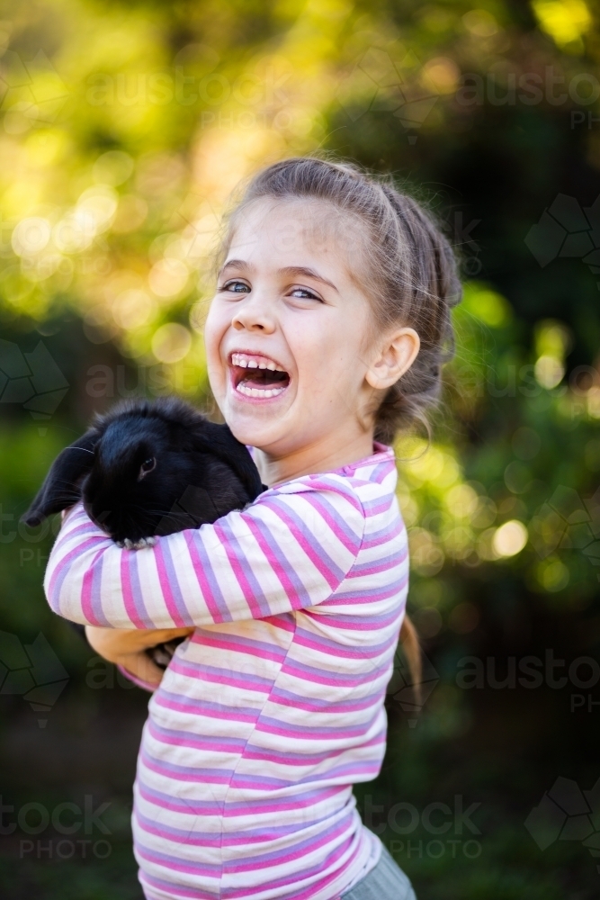 Happy young kid laughing and cuddling black pet bunny rabbit - Australian Stock Image