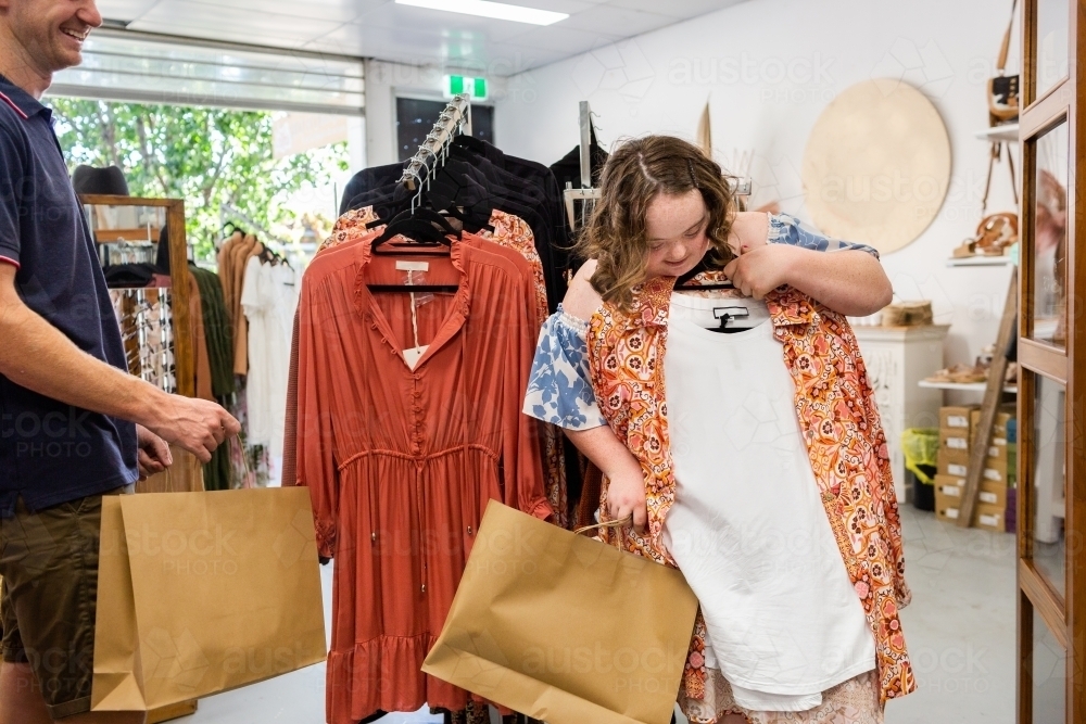 Happy young lady with down syndrome shopping in dress and clothing store boutique - Australian Stock Image