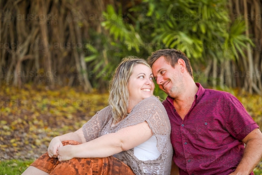 Happy young romantic couple sitting together in golden afternoon light at the park - Australian Stock Image