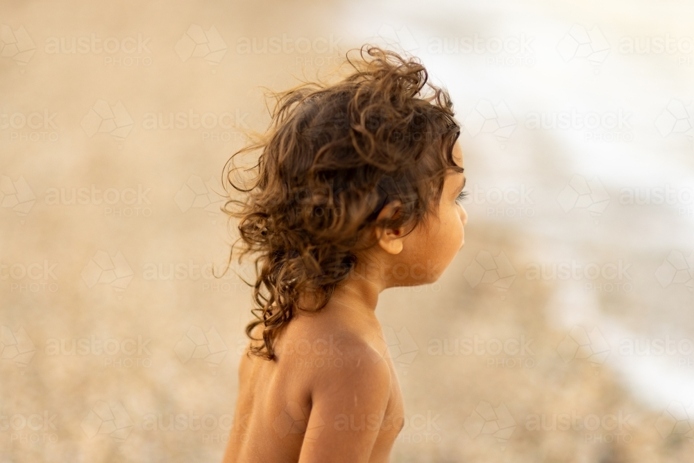 head and shoulders of aboriginal child with tousled windswept hair looking away - Australian Stock Image