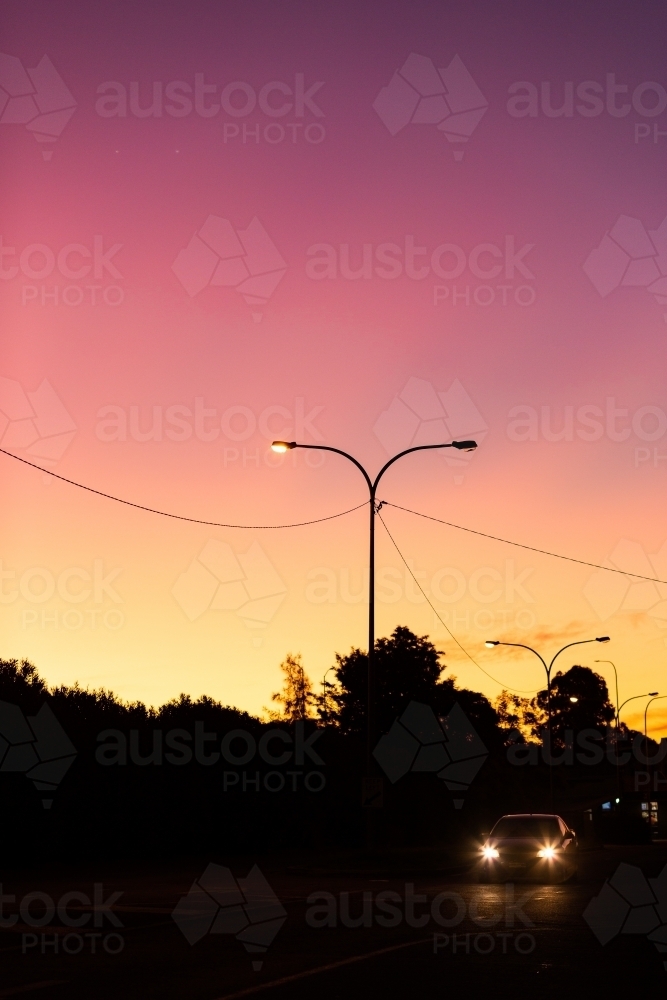 headlights of car driving on dark street at night with dusk silhouettes - Australian Stock Image