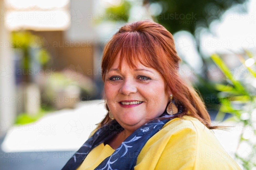 Headshot of happy smiling middle age woman wearing yellow in urban setting - Australian Stock Image