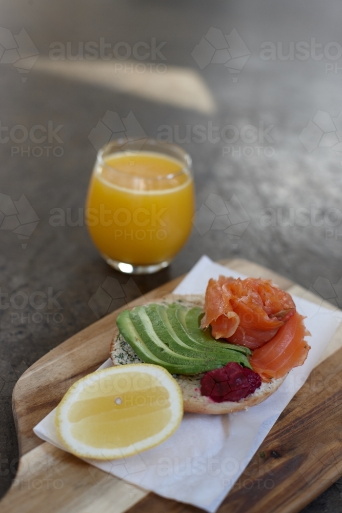 Healthy salmon and avocado bagel meal on wooden chopping block - Australian Stock Image