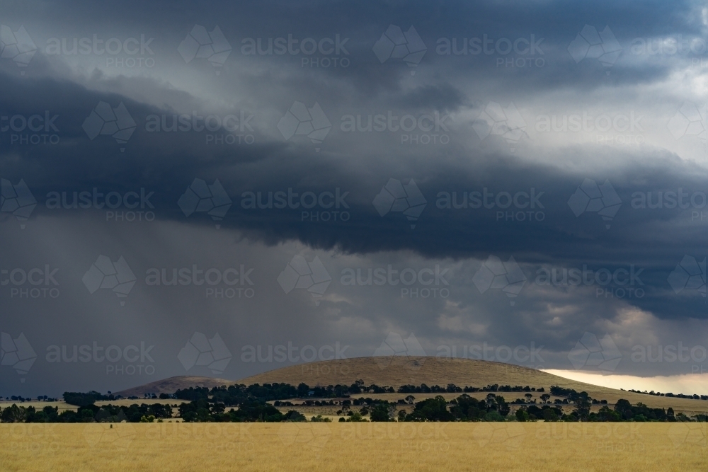 Heavy rain and a dark shelf cloud over a dry barren hill on rural farmland - Australian Stock Image