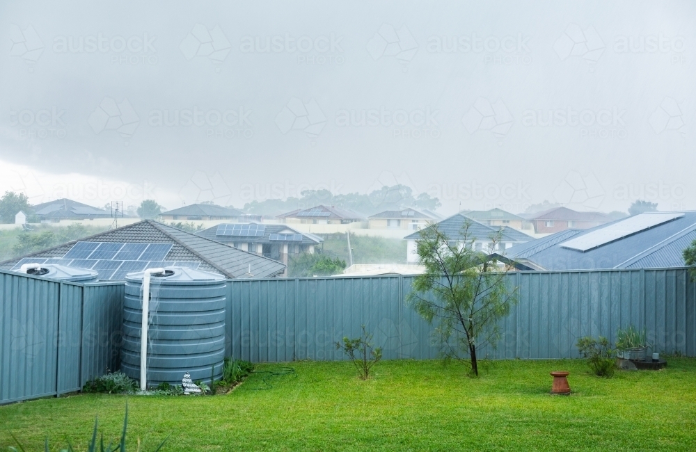 Heavy rainfall in backyard with water overflowing from tank - Australian Stock Image