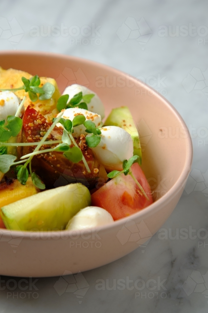 Heirloom tomatoes salad with mozzarella cheese in a pink bowl - Australian Stock Image