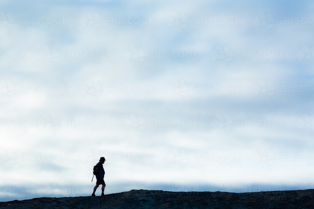 Hiker walking along ridge with soft cloudy sky background - Australian Stock Image