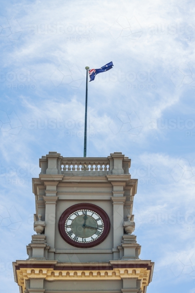 Historic clock tower flying an Australian flag against a blue sky - Australian Stock Image