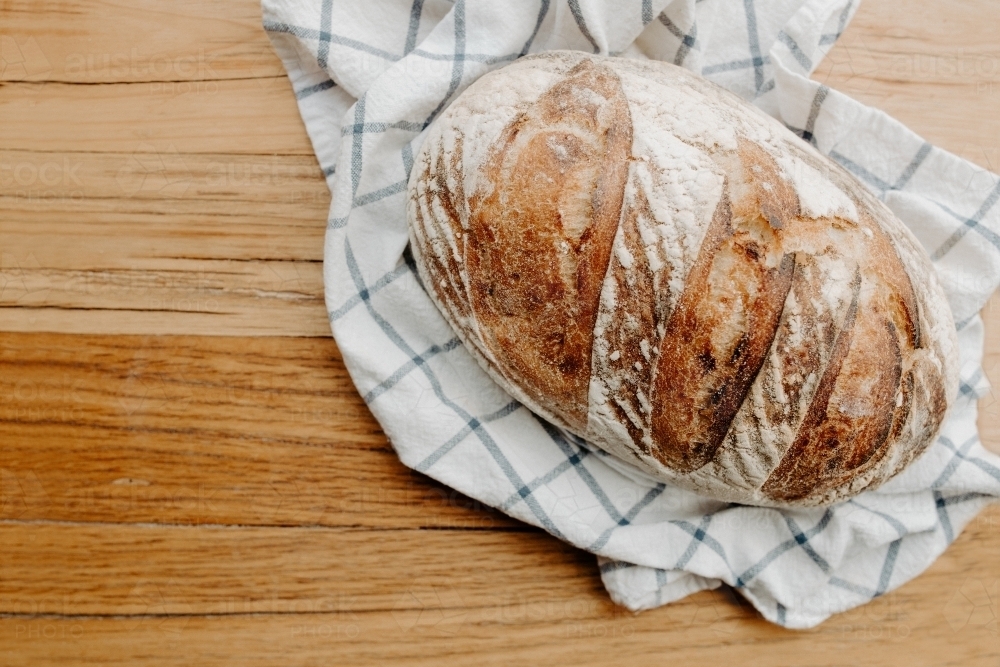 Home made Sour dough bread cooling on a tea towel which is on a wooden chopping platter board - Australian Stock Image