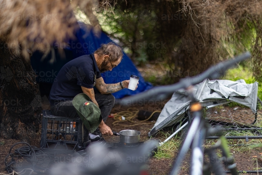 Homeless man pouring water from his camp stove into a cup - Australian Stock Image