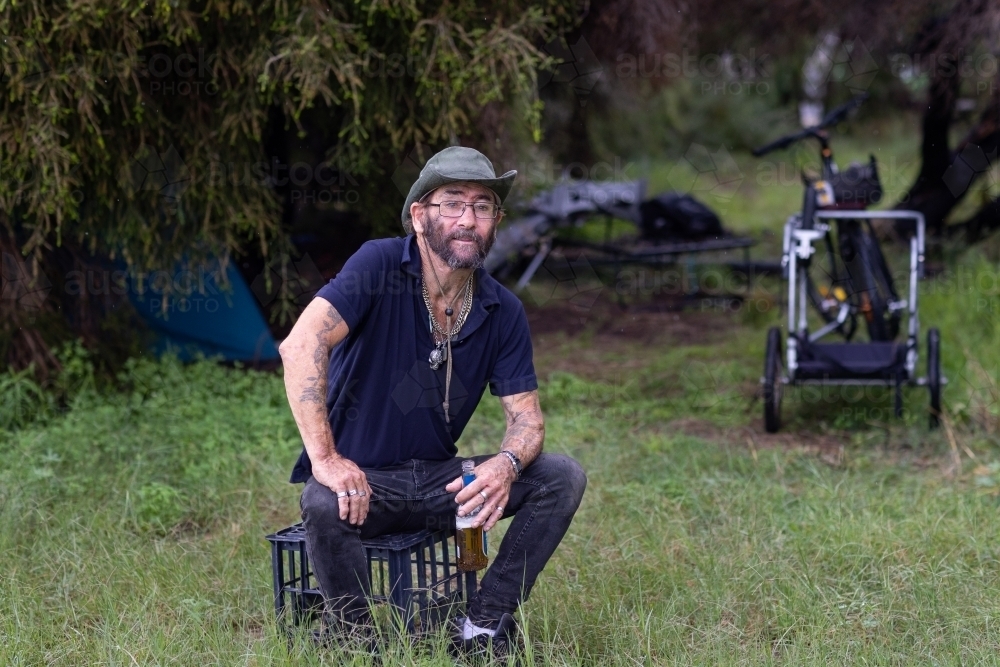 Homeless man with a beer sitting on a milk crate in the bush - Australian Stock Image