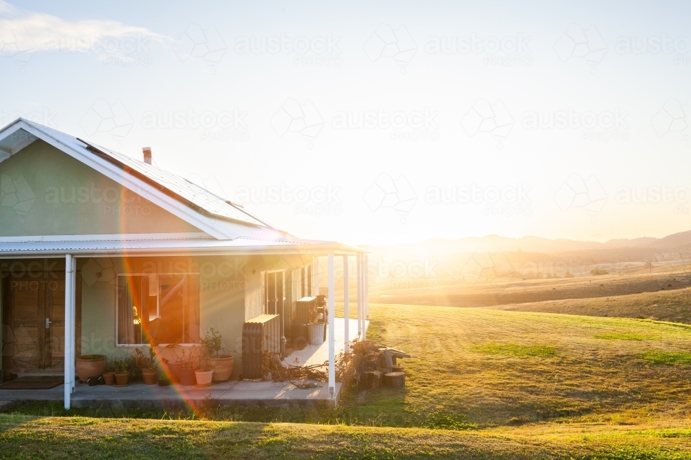 Homestead on hilltop with last rays of sunlight shining over scene and solar panels on roof - Australian Stock Image