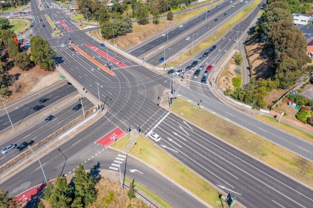 Horizontal aerial view of a freeway overpass with cars, trees, and buildings on a sunny day - Australian Stock Image