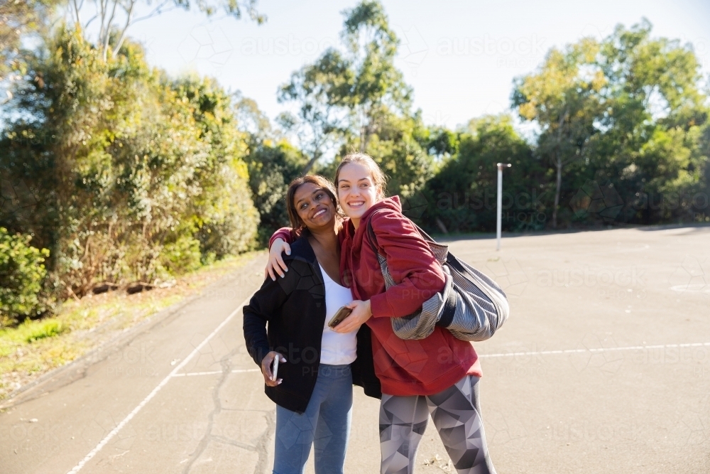 horizontal photo of two young women wearing coat and jacket close to each other on a sunny day - Australian Stock Image