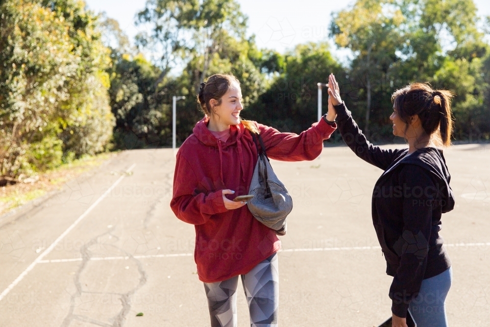 horizontal photo of two young women wearing coat and jacket holding each others hands on a sunny day - Australian Stock Image