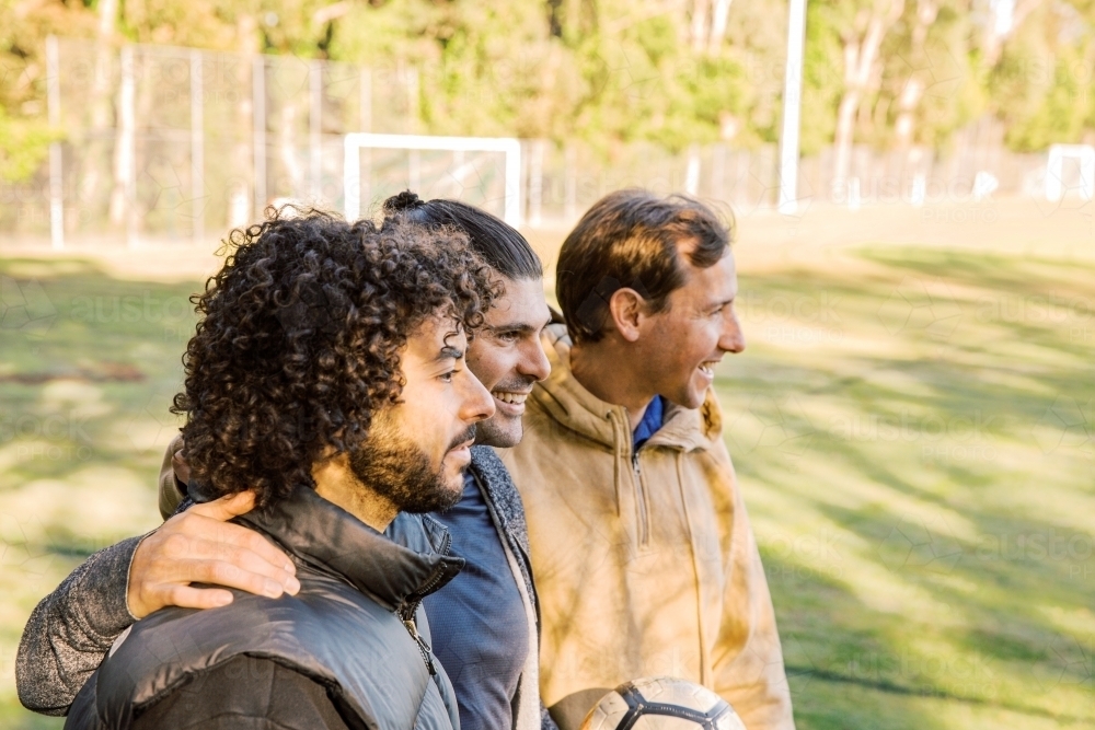 Horizontal shot of 3  interracial men smiling standing on a soccer field - Australian Stock Image