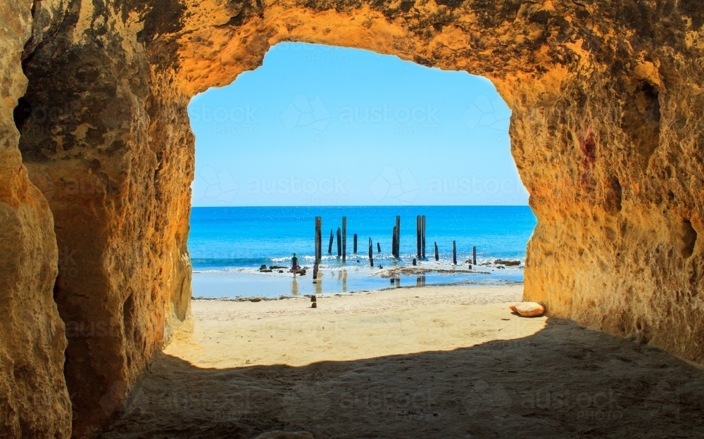 Horizontal shot of a beach cave toward bright blue water on a sunny day - Australian Stock Image