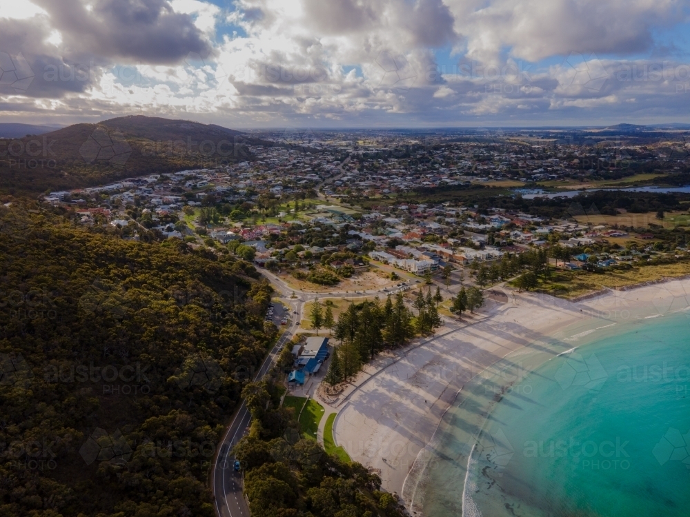 horizontal shot of a beach with white sand, mountains, shadows of trees, buildings and cloudy skies - Australian Stock Image