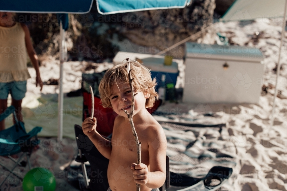 Horizontal shot of a boy on the beach holding twigs on his hand - Australian Stock Image