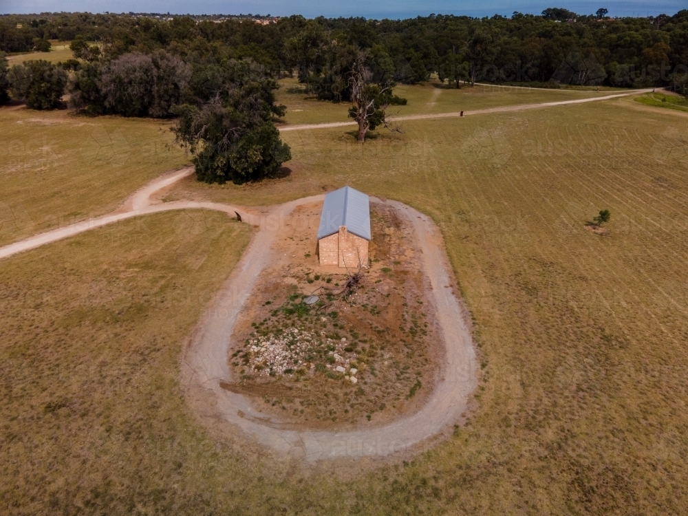 horizontal shot of a farmhouse with a road around it and with trees in the background under blue sky - Australian Stock Image