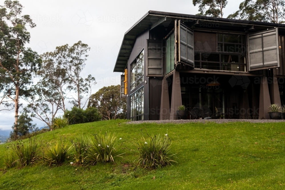 horizontal shot of a house with open windows, trees and bushes with white flowers - Australian Stock Image