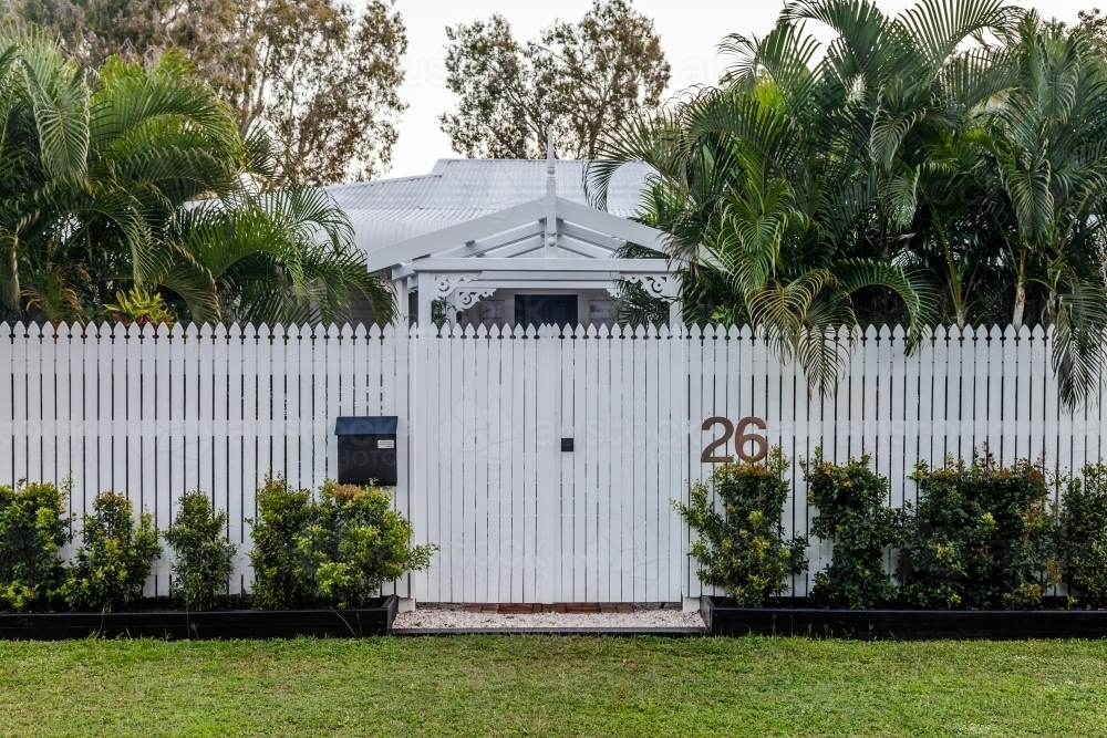 horizontal shot of a house with white fence, grass, bushes and trees - Australian Stock Image