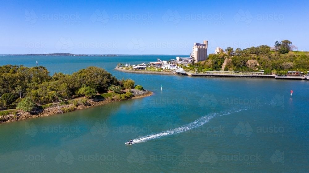 Horizontal shot of a jetski heading to the left away from industry - Australian Stock Image