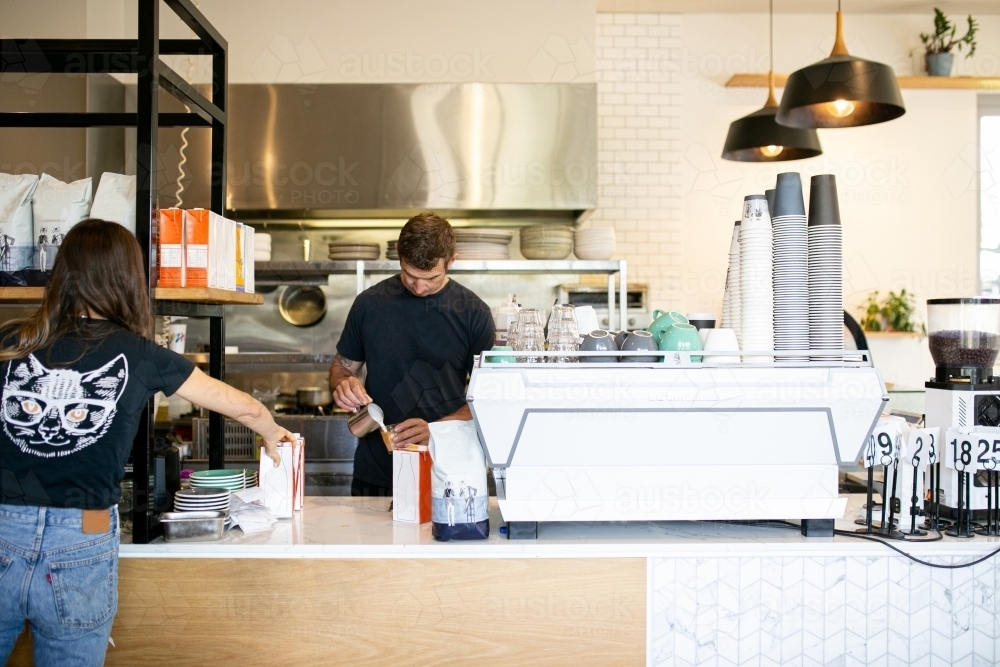 horizontal shot of a man mixing a drink while the woman is reaching for something at the counter - Australian Stock Image