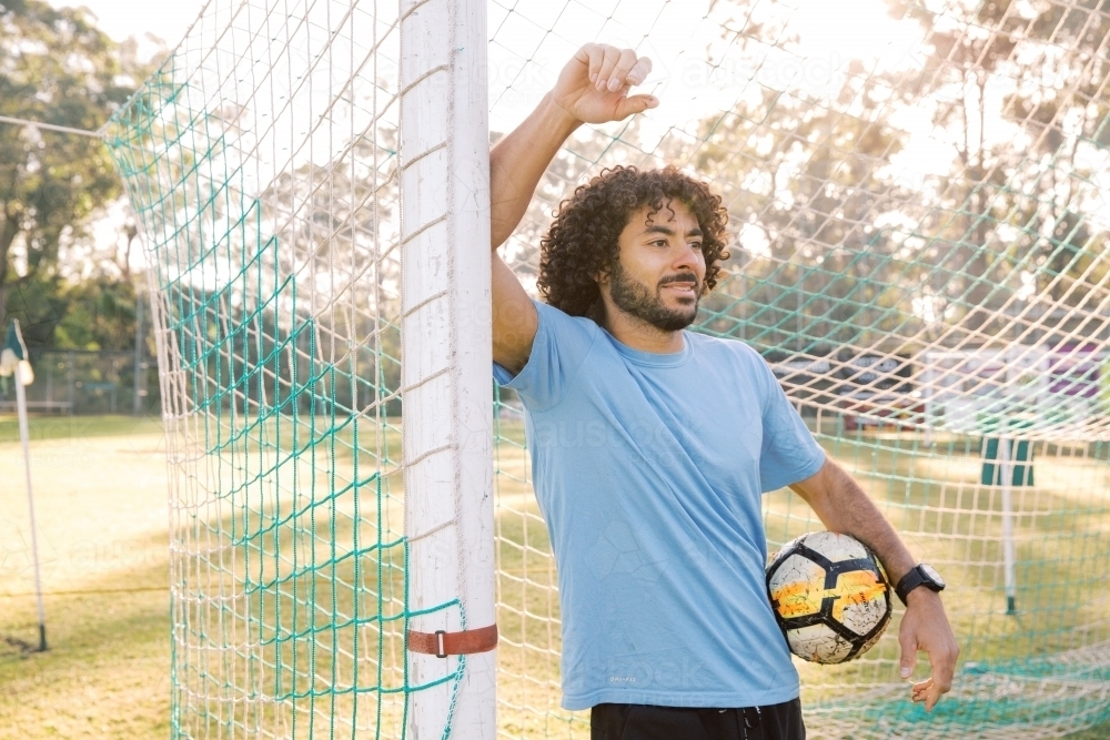 horizontal shot of a man standing against a goal with one arm raised and the other holding a ball - Australian Stock Image