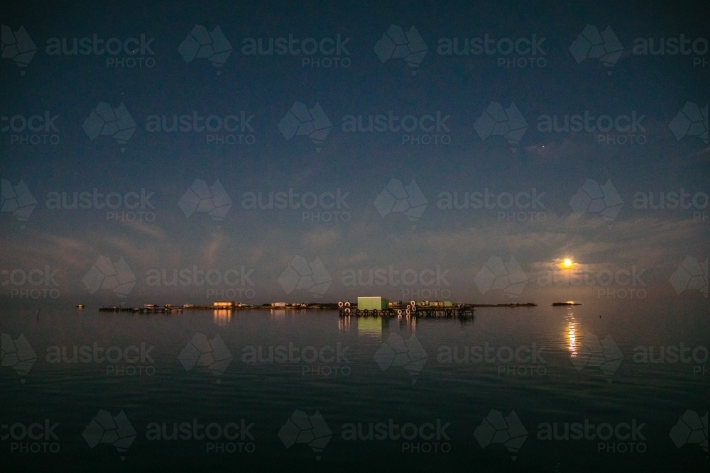 Horizontal shot of a moon setting over an island. - Australian Stock Image