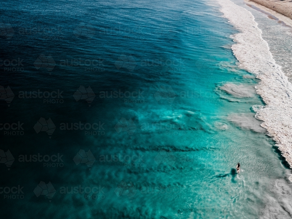 horizontal shot of a person paddling on the beach with waves on a sunny day with clear skies - Australian Stock Image