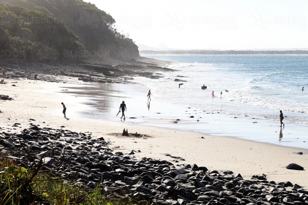 horizontal shot of a remote beach with people, mountains, rocks and waves on a sunny day - Australian Stock Image