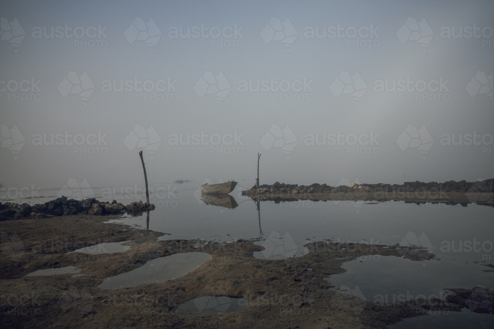 Horizontal shot of a row boat on an inlet in a misty morning - Australian Stock Image