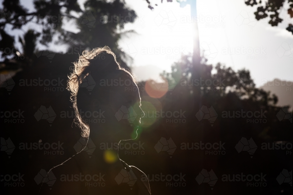 horizontal shot of a silhouette of woman with trees and sunlight in the background - Australian Stock Image