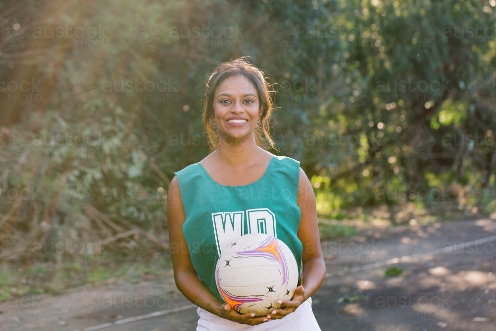 horizontal shot of a tanned skin woman in sports in wear holding a net ball on a sunny day - Australian Stock Image