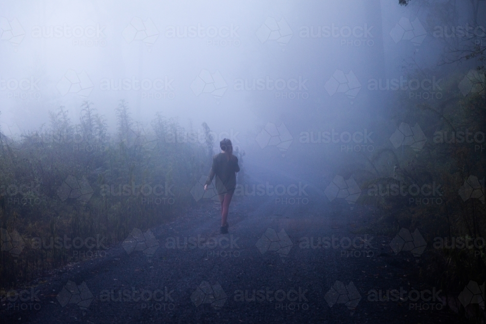 horizontal shot of a woman walking on a misty road with trees and bushes - Australian Stock Image