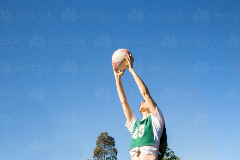 horizontal shot of a young woman holding a ball up high in the air on a sunny day with clear skies - Australian Stock Image